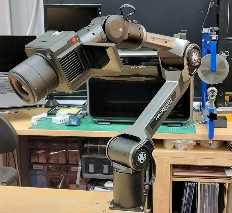 The arm on the bench, reaching out over the work surface with a cinema camera mounted at the wrist